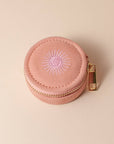 Pink round jewelry case with gold zipper on a beige background