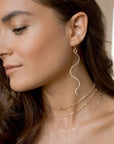 Model wearing 14k gold Sidewinder earrings. These sidewinders feature a snake like look to them with a hook earring.