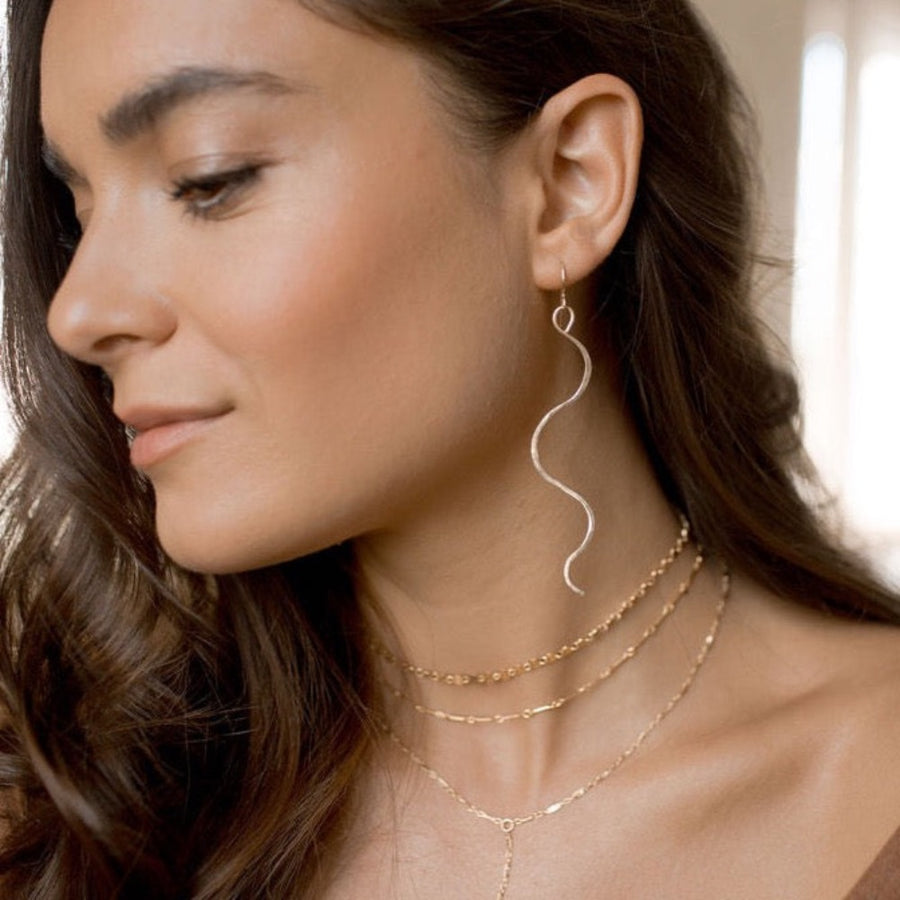 Model wearing 14k gold Sidewinder earrings. These sidewinders feature a snake like look to them with a hook earring.