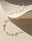 925 Sterling Silver Petite heart chain from Token Jewelry, photographed on a white, organically shaped ceramic dish. This chain features a silver tiny heart wire throughout the whole chain. 
