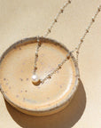 925 sterling silver beaded chain with a pretty single pearl necklace laid on a ceramic dish in the sunlight. 