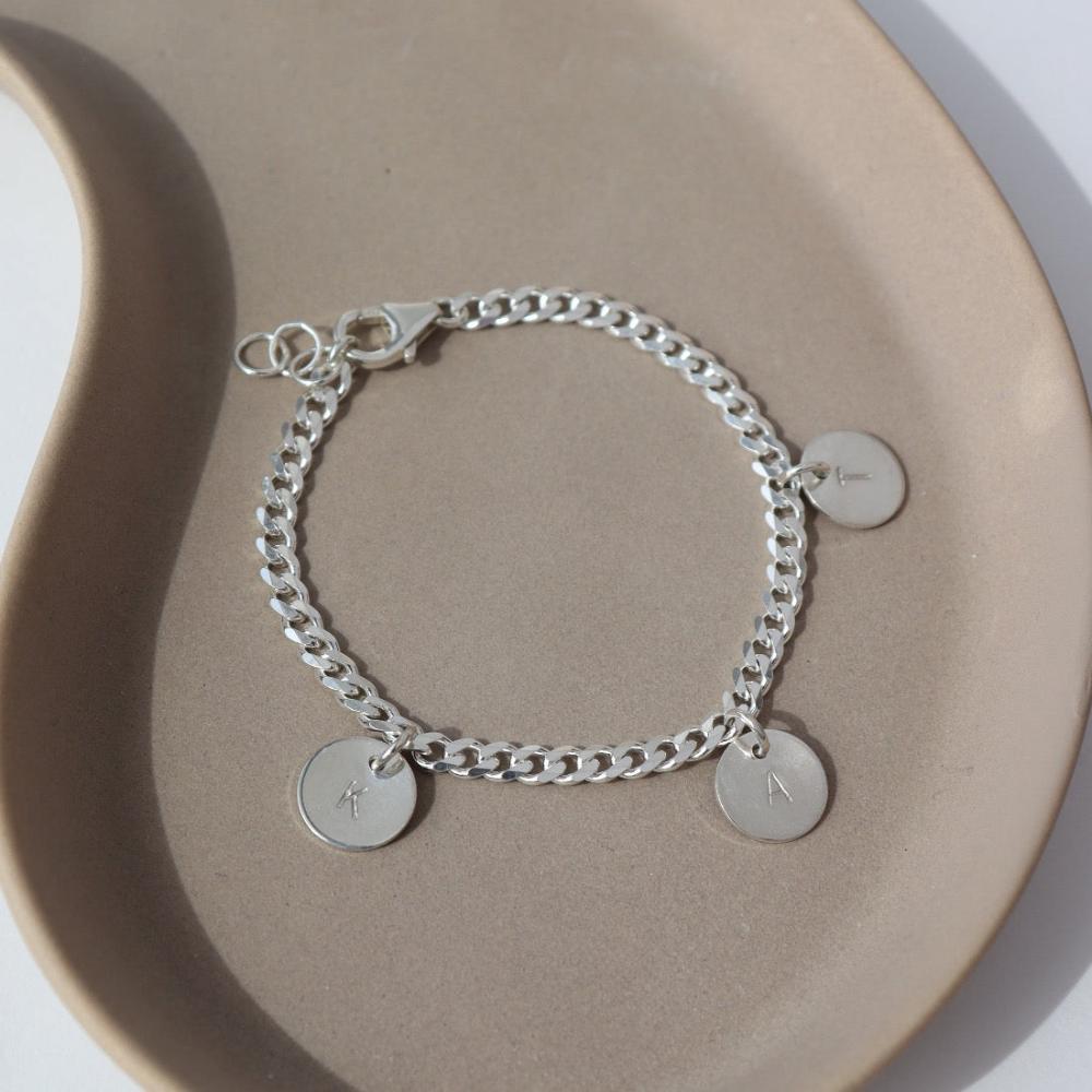 925 sterling silver Carter Personalized disc Bracelet laid on a gray plate in the sunlight. This bracelet features the Carter chain then followed Initial stamped disc.