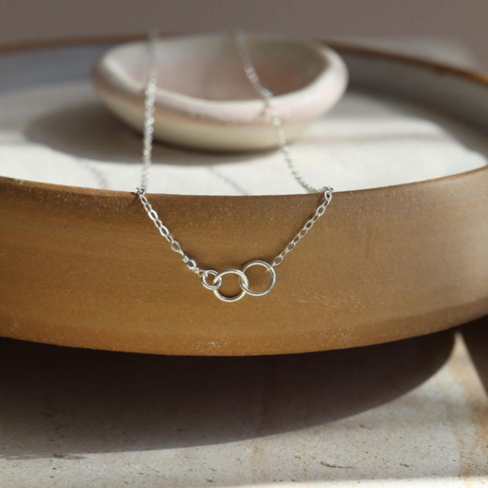 14k gold fill Lineage Necklace placed on a white jewelry dish. This necklace features jump rings representing parents, kids, and others you are able to pick the sizing of each jump ring.