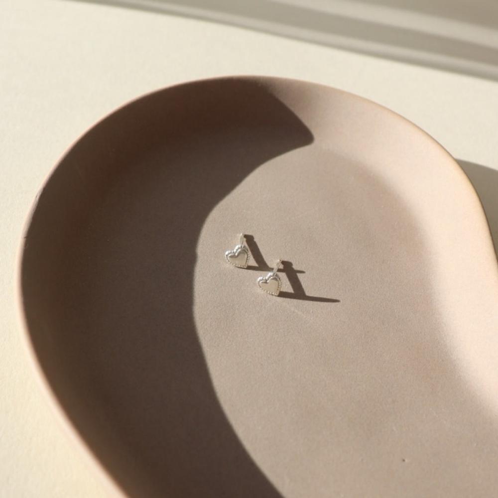 small sterling silver heart studs with a patterned border, on a ceramic dish