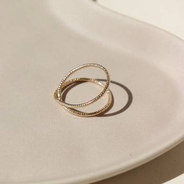14k gold fill Sunburst Infinity ring laid on a tan plate In the sunlight.