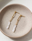 14k gold fill Lucy Drop earrings laid on a tan plate in the sunlight. These earrings feature a stud earring with a chain link dangle followed by two rainbow moonstone gemstones.