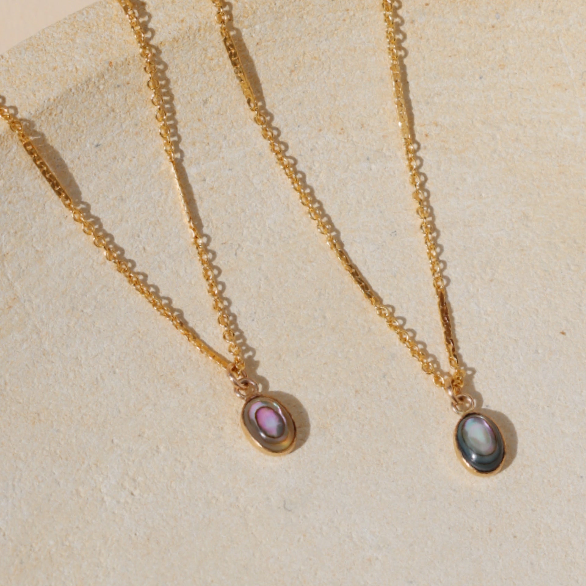 2 chain necklaces with abalone pendant charms on a light dish