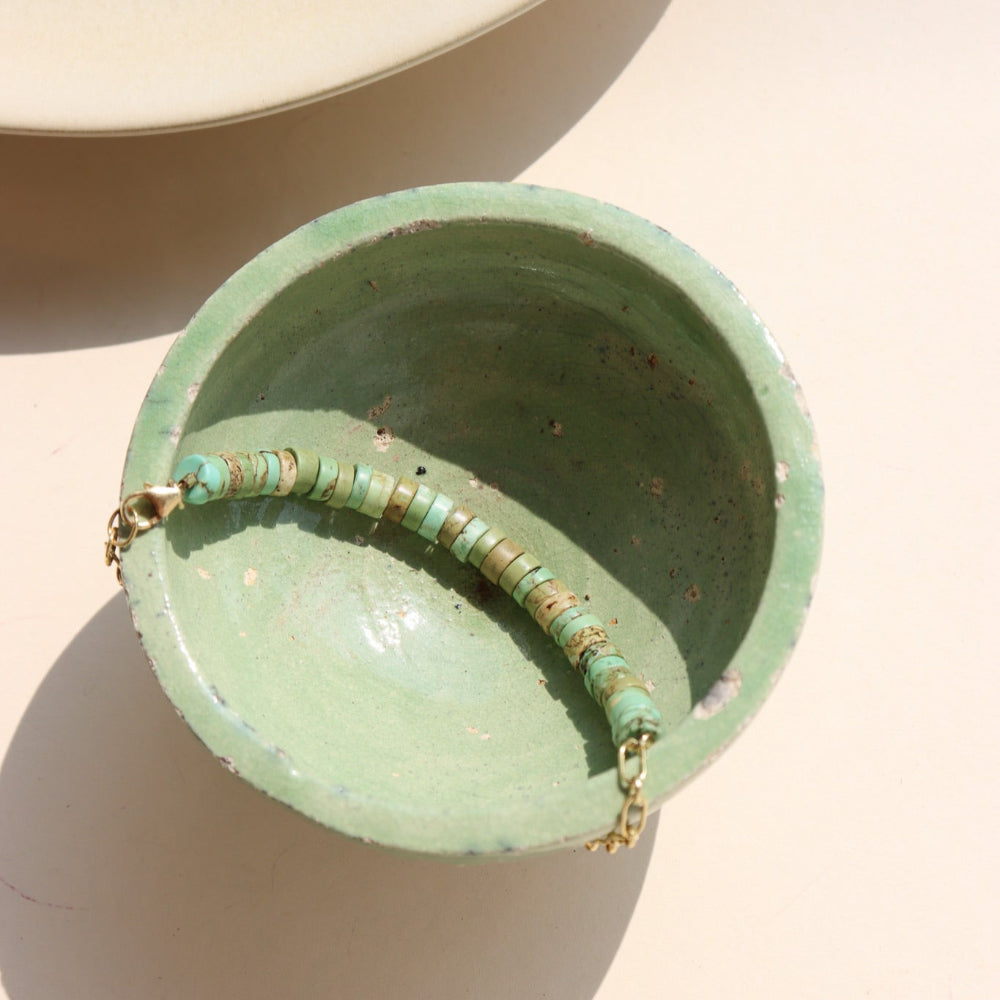 A 14k gold fill beaded anklet with a chain link style chain, draped over a green dish in the sunlight 
