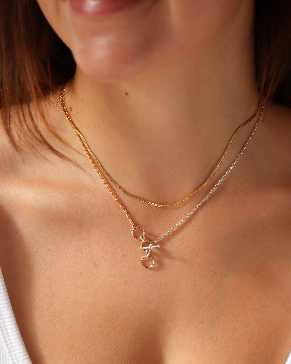 Model wearing a delicate gold layering chain with a mixed-metal gold and sterling silver toggle necklace featuring circular links.