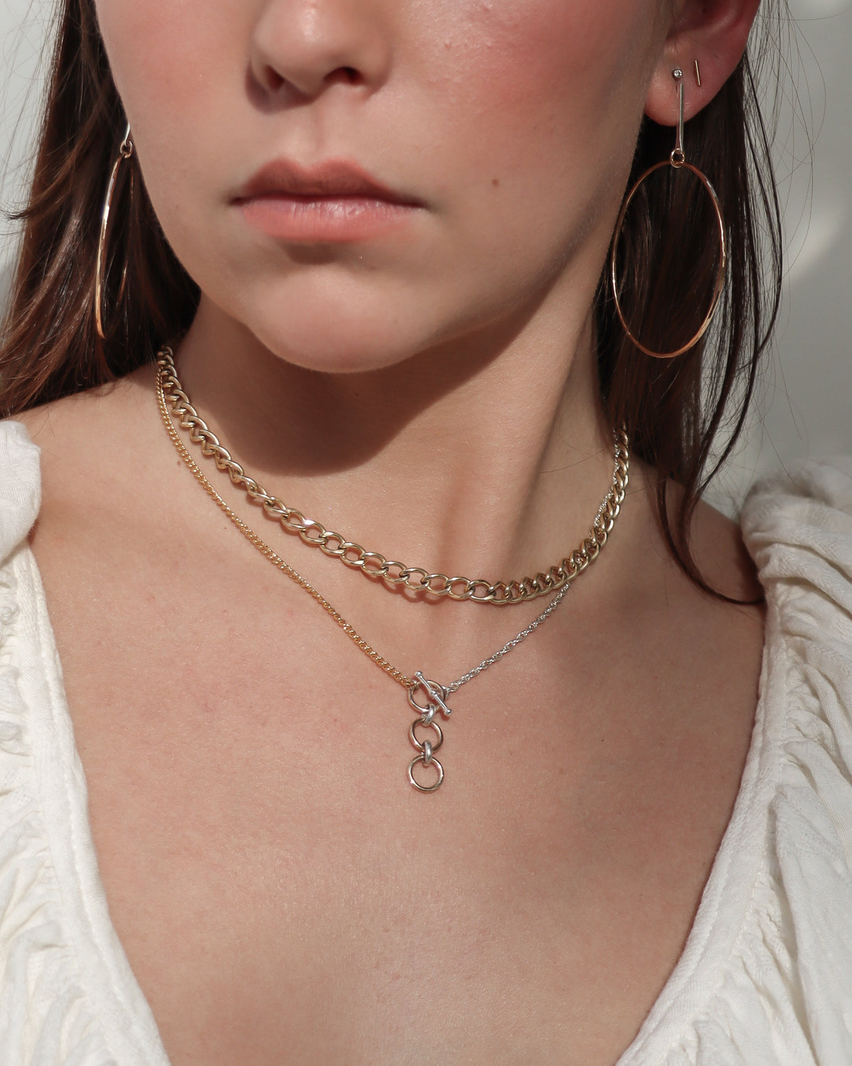Angled close-up of layered gold and silver necklaces on a model, highlighting a mixed-metal toggle clasp with dangling circular accents.