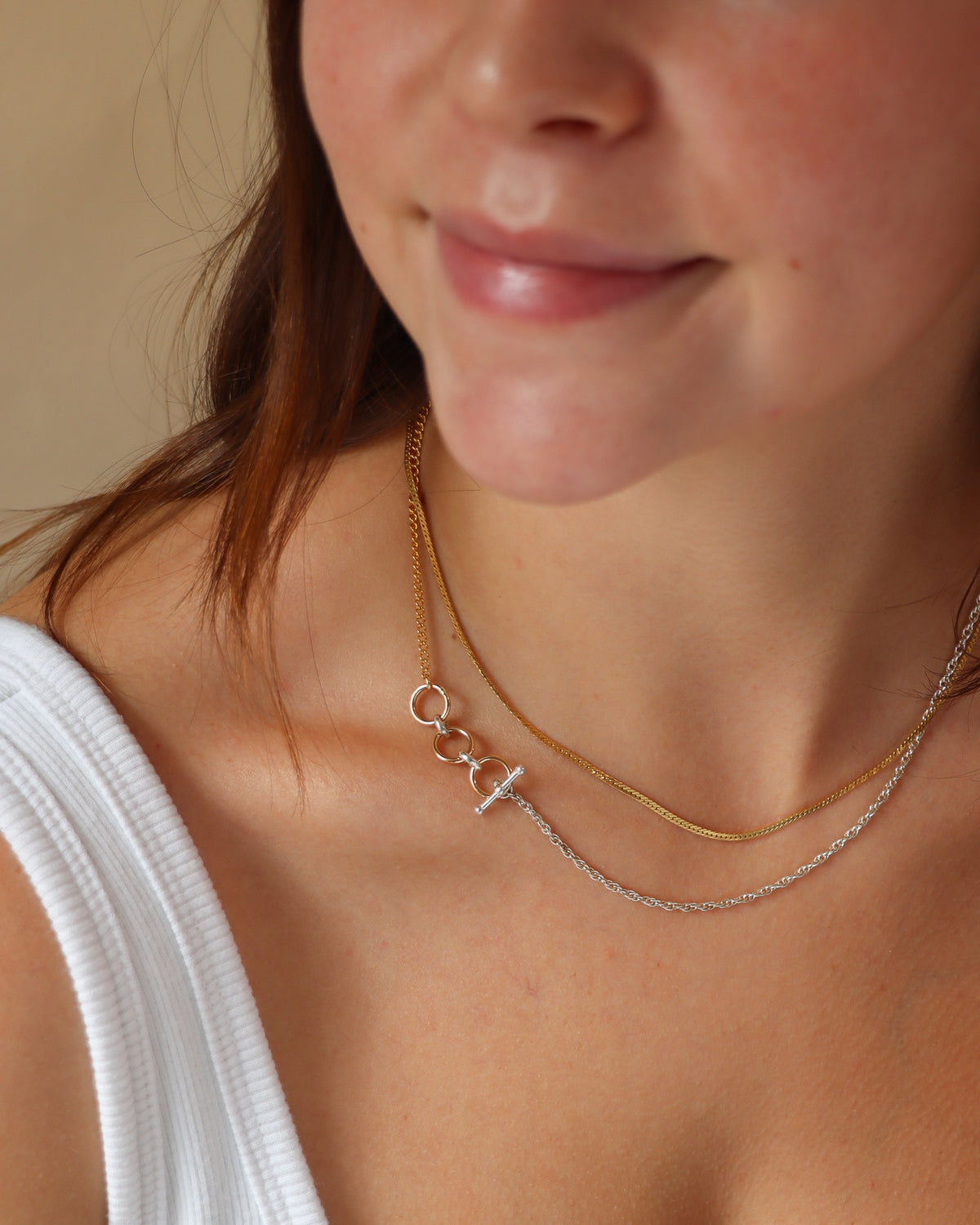 Close-up of a model wearing layered gold and silver chain necklaces, featuring a mixed-metal design with interlocking circular links and a silver toggle clasp.