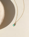 A 6x8mm Amazonite Gemstone set in a 14k gold fill bezel. The necklace features a thin standard chin. Necklace is displayed on a cream back drop in the sunlight. 