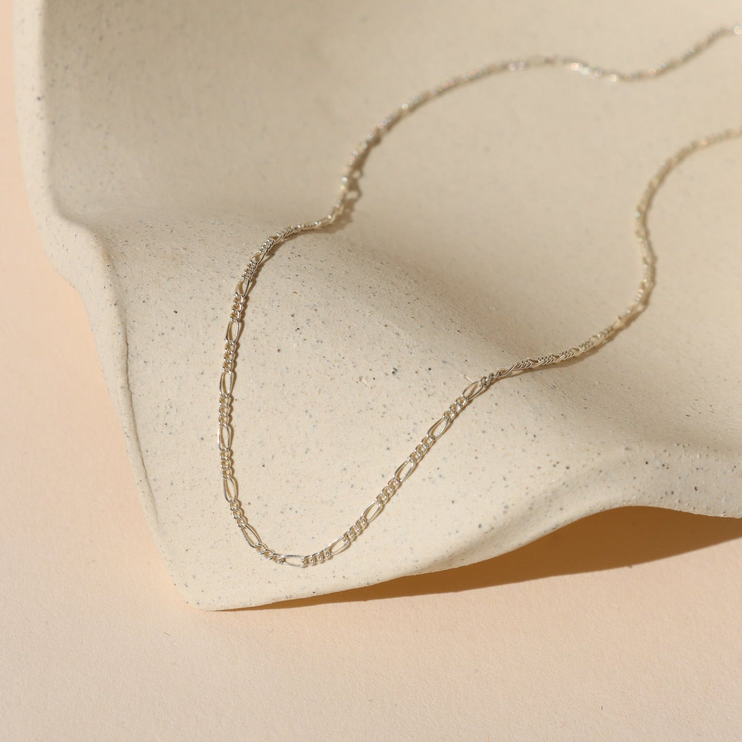 sterling silver figaro chain necklace on a light dish