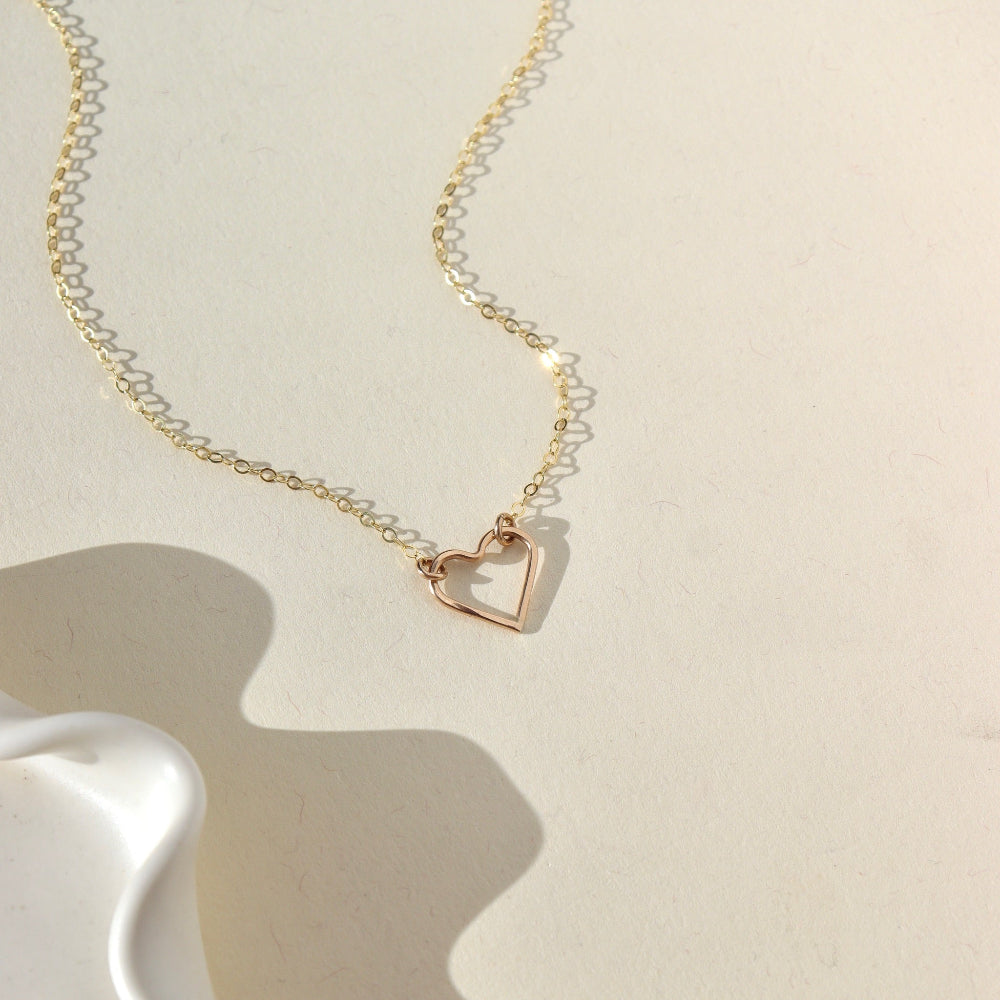 A 14k gold fill necklace featuring a thin standard chain with an open heart pendant anchored at the end. 