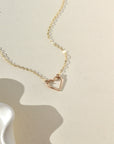 A 14k gold fill necklace featuring a thin standard chain with an open heart pendant anchored at the end. 