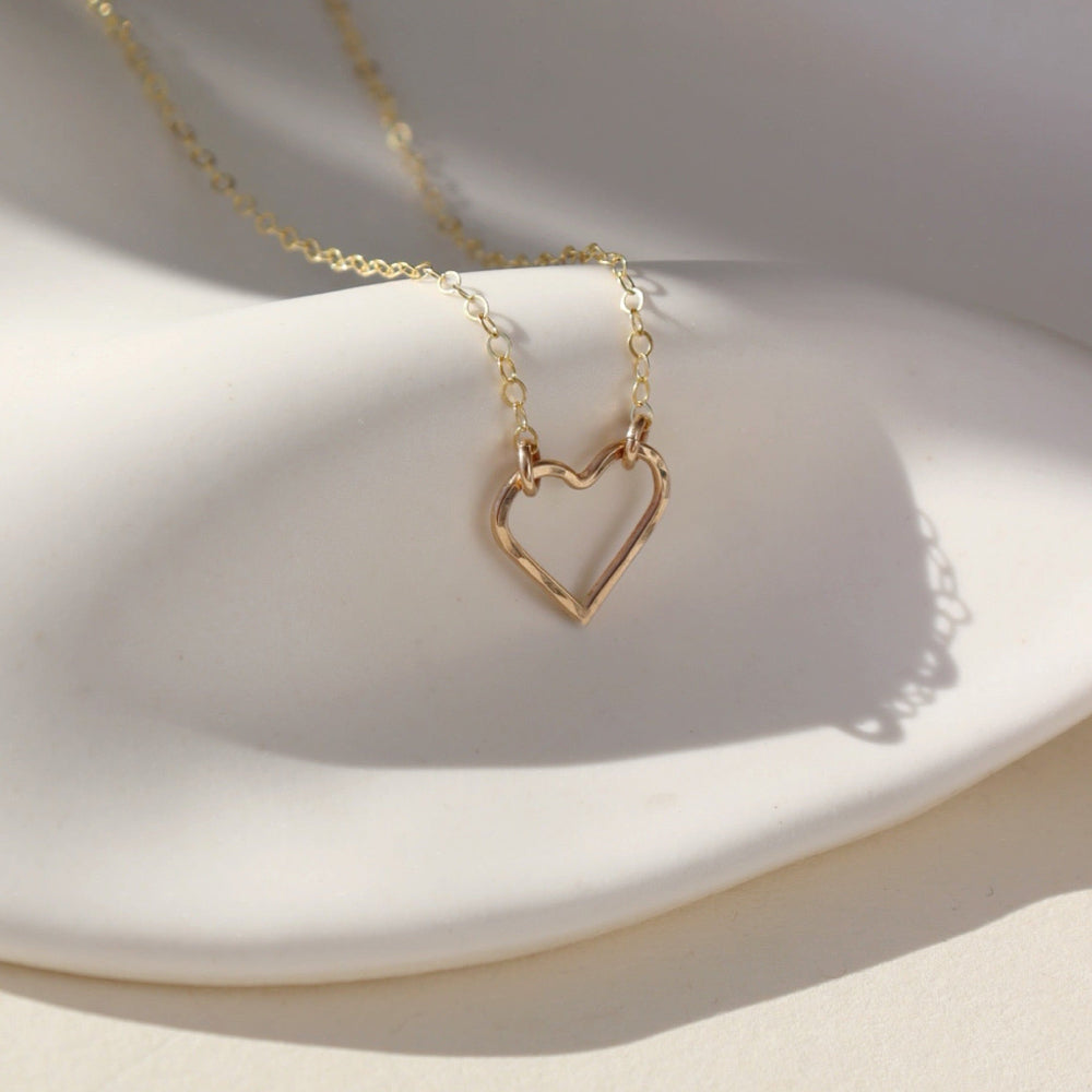 A 14k gold fill necklace featuring a thin standard chain with an open heart pendant anchored at the end. 