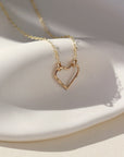 A 14k gold fill necklace featuring a thin standard chain with an open heart pendant anchored at the end. 