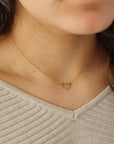 Model wearing a 14k gold fill necklace featuring a thin standard chain with an open heart pendant anchored at the end. 