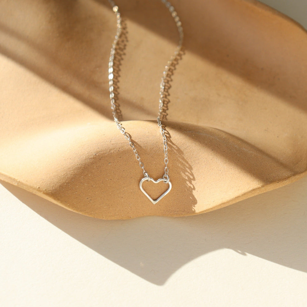 A sterling silver necklace featuring a thin standard chain with an open heart pendant anchored at the end. 