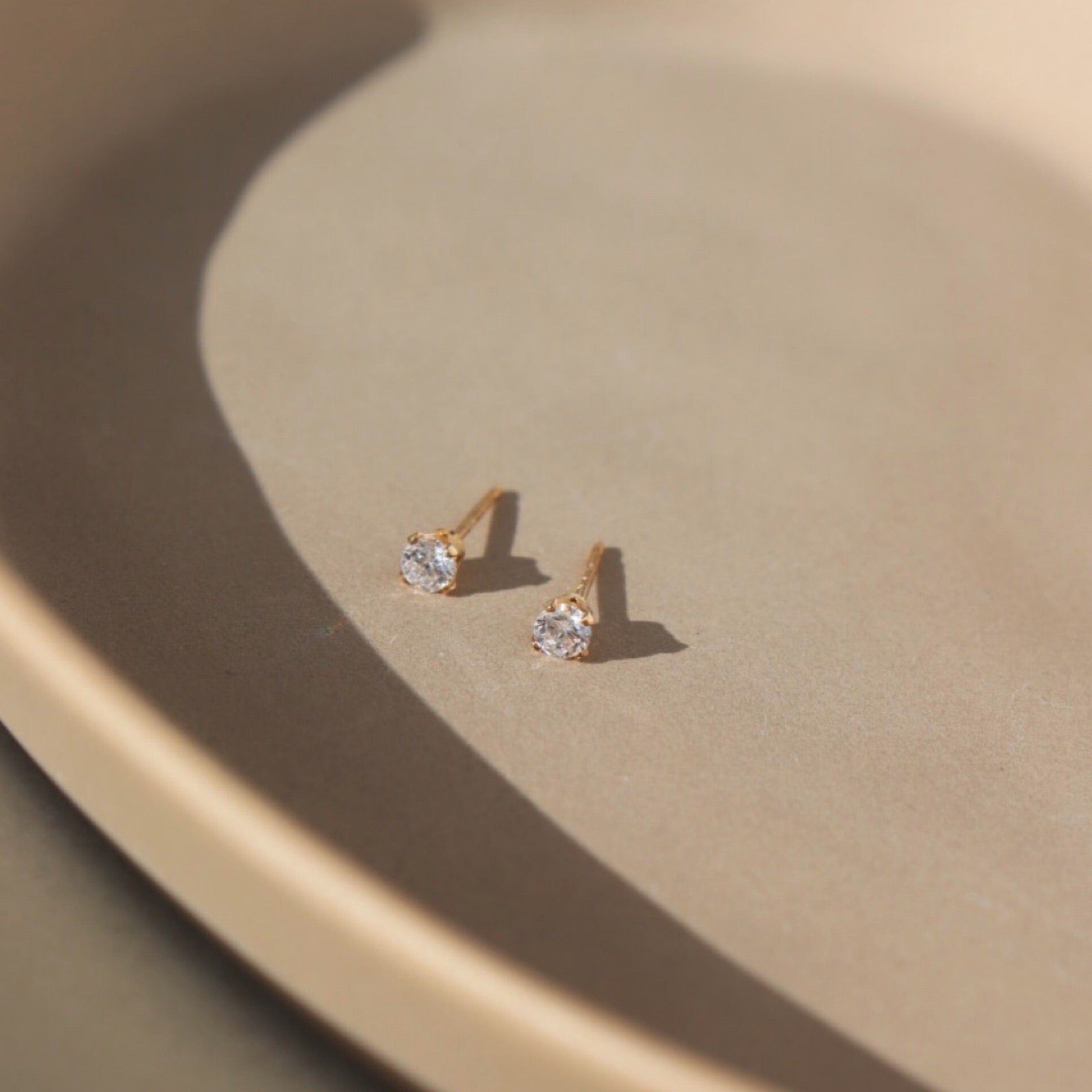 Stud earring placed on top of a tan plate. The studies featuring bright cubic zirconia gemstones. 14k gold fill studs made for everyday wear.