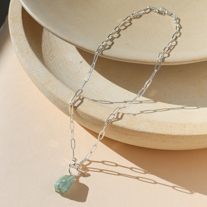 sterling silver chain necklace with a toggle clasp that has an aquamarine stone on a light dish