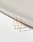 14k solid gold wire formed into arch shaped earrings with one hammered end, photographed on a white table leaning on a white dish