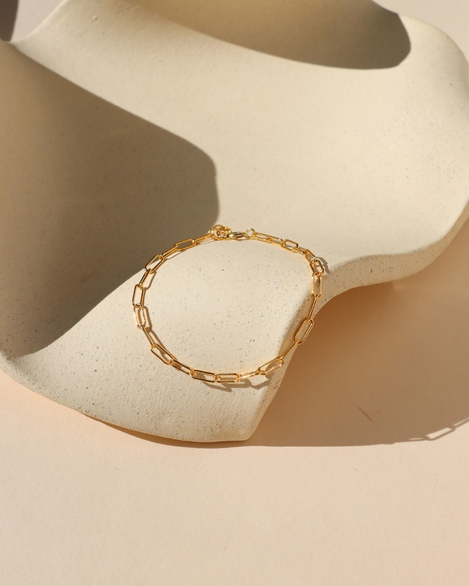 gold paperclip chain bracelet in the sunlight on a wavy dish