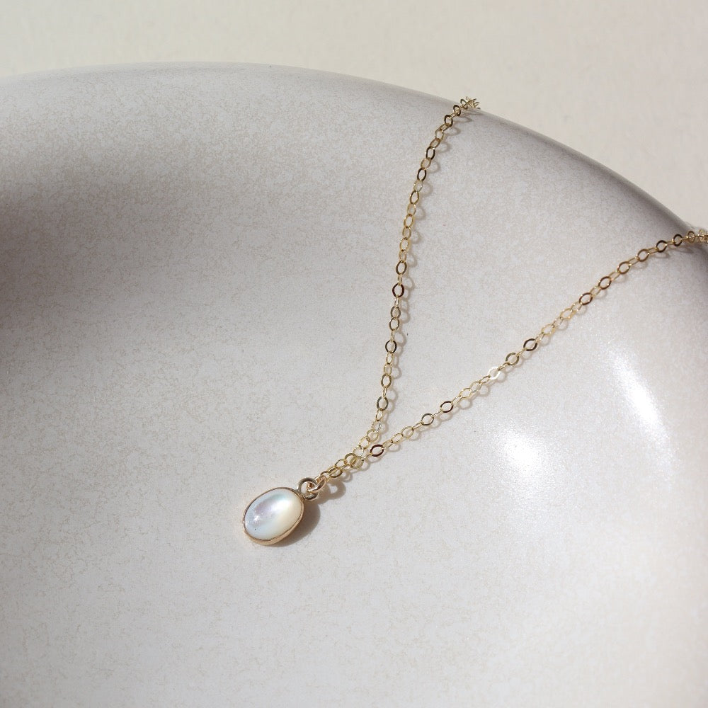 mother of pearl bezel pendant on a 14k gold fill delicate chain, photographed on a white ceramic dish