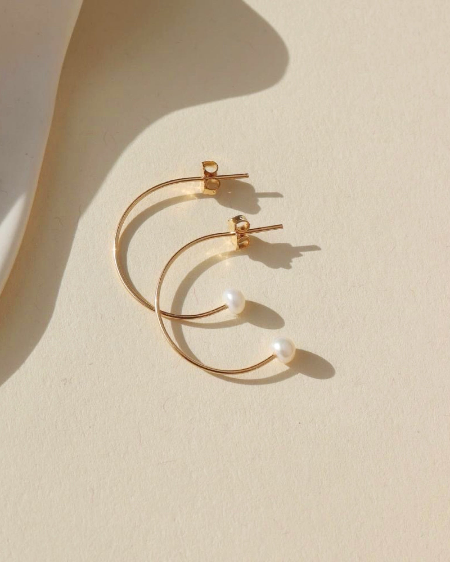 14k gold fill wire hoop earrings with pearls on the ends on a light background
