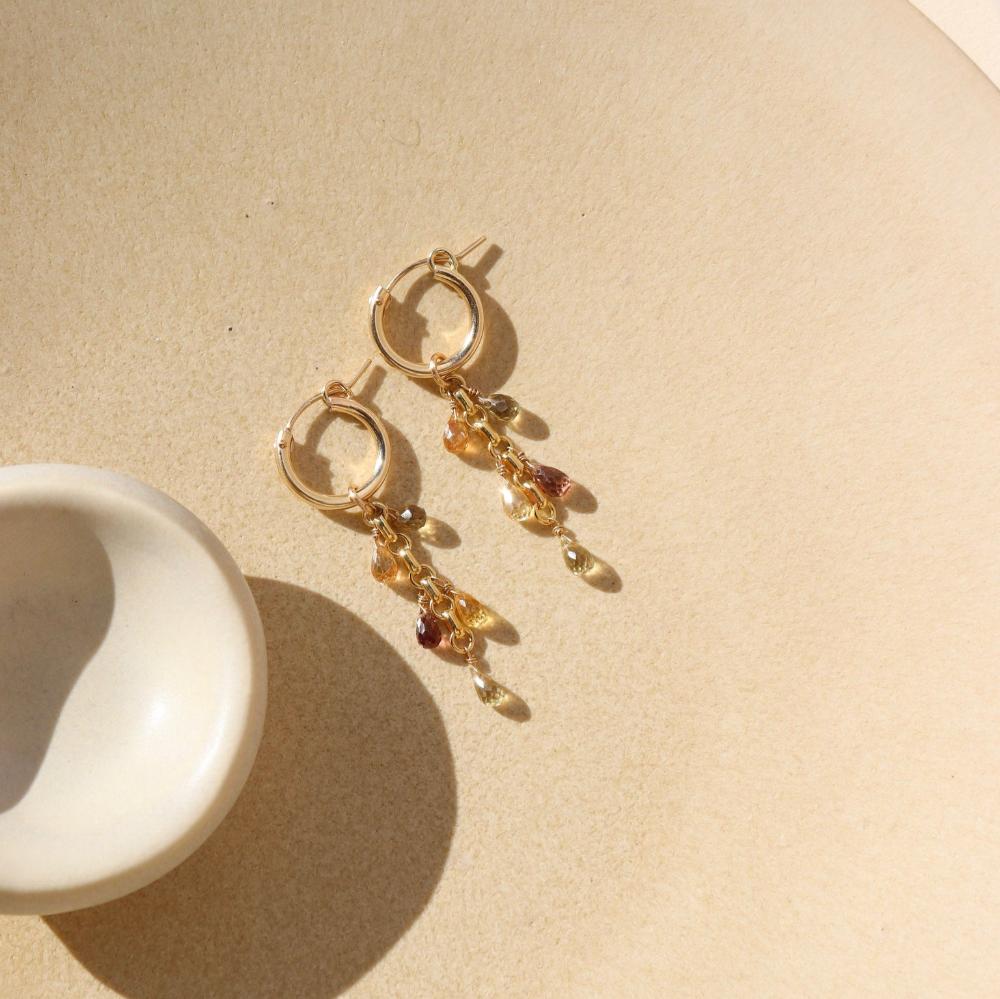 Small gold hoop with 5 zircon faceted teardrop stones on each earring. Earrings are displayed on tan dish. 