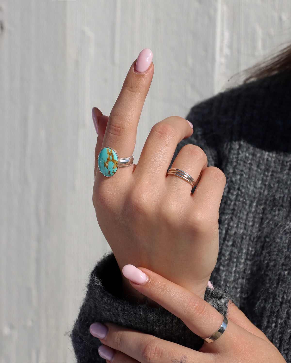 Close-up of a hand wearing a statement turquoise ring with natural brown matrix in a sterling silver setting, paired with minimalist silver stacking rings and a hammered silver band.