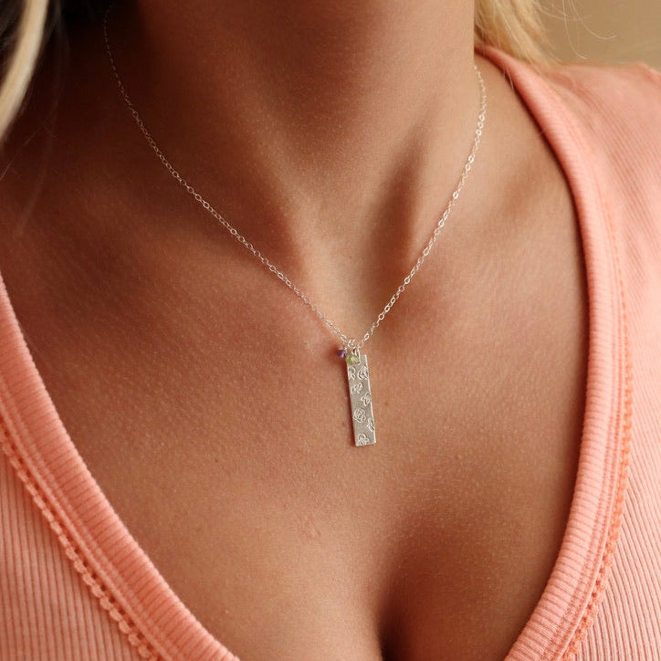 model wearing sterling silver delicate chain necklace with hand stamped birth flowers on a bar pendant