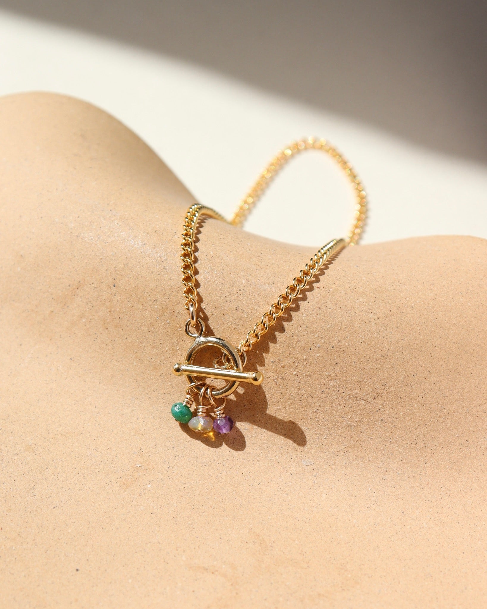 A simple 14k gold fill toggle featuring three tiny birthstone charms, dangling from a small toggle on a curb chain. The bracelet is displayed orange dish. 