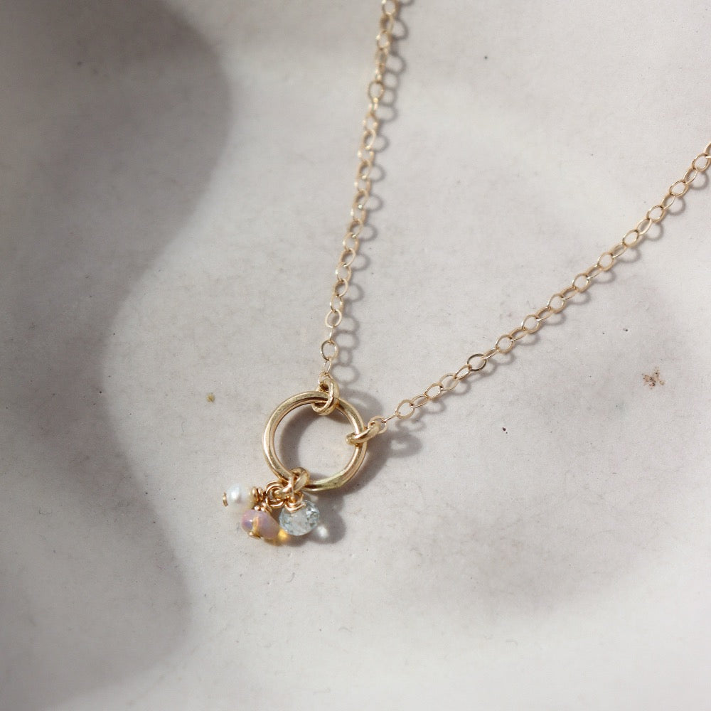 14k solid gold necklace made by Token Jewelry, featuring a simple chain and circle, with customizable birthstone charms, photographed on a white dish