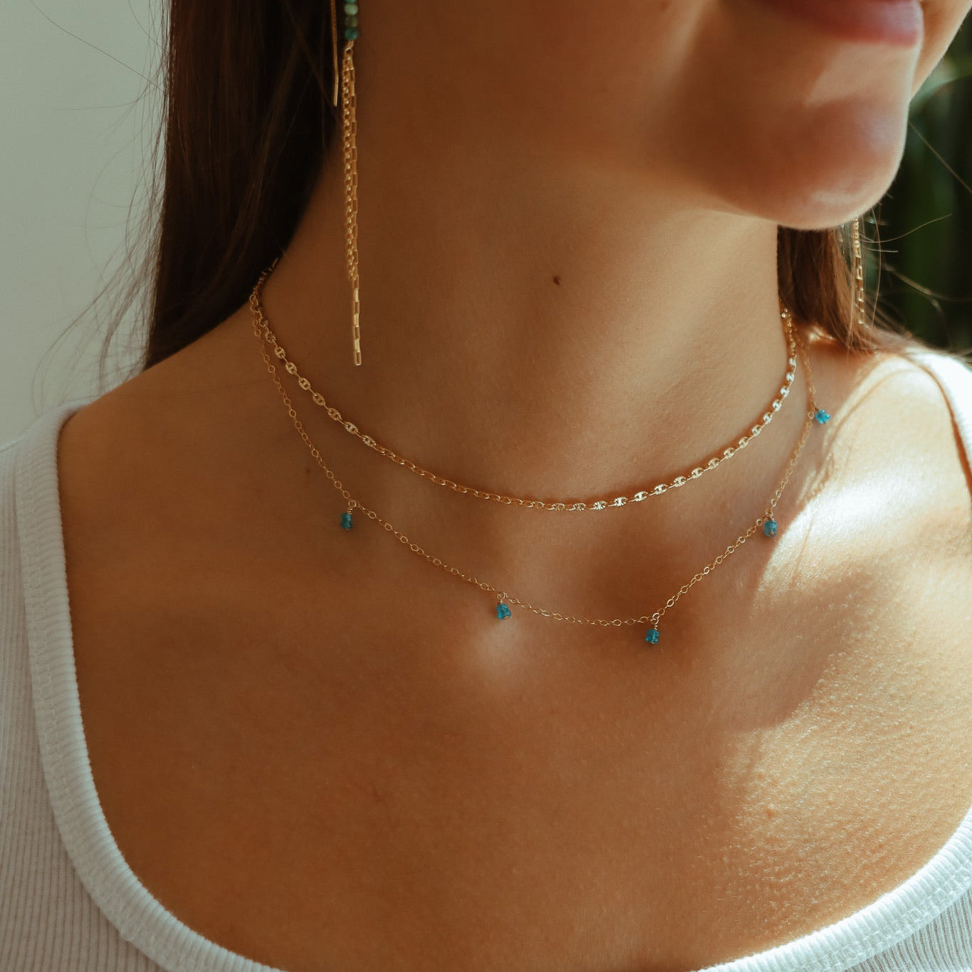 Model wearing the bluebell necklace featuring blue apatite gemstones dangling from a simple chain layered with other 14k gold filled jewelry