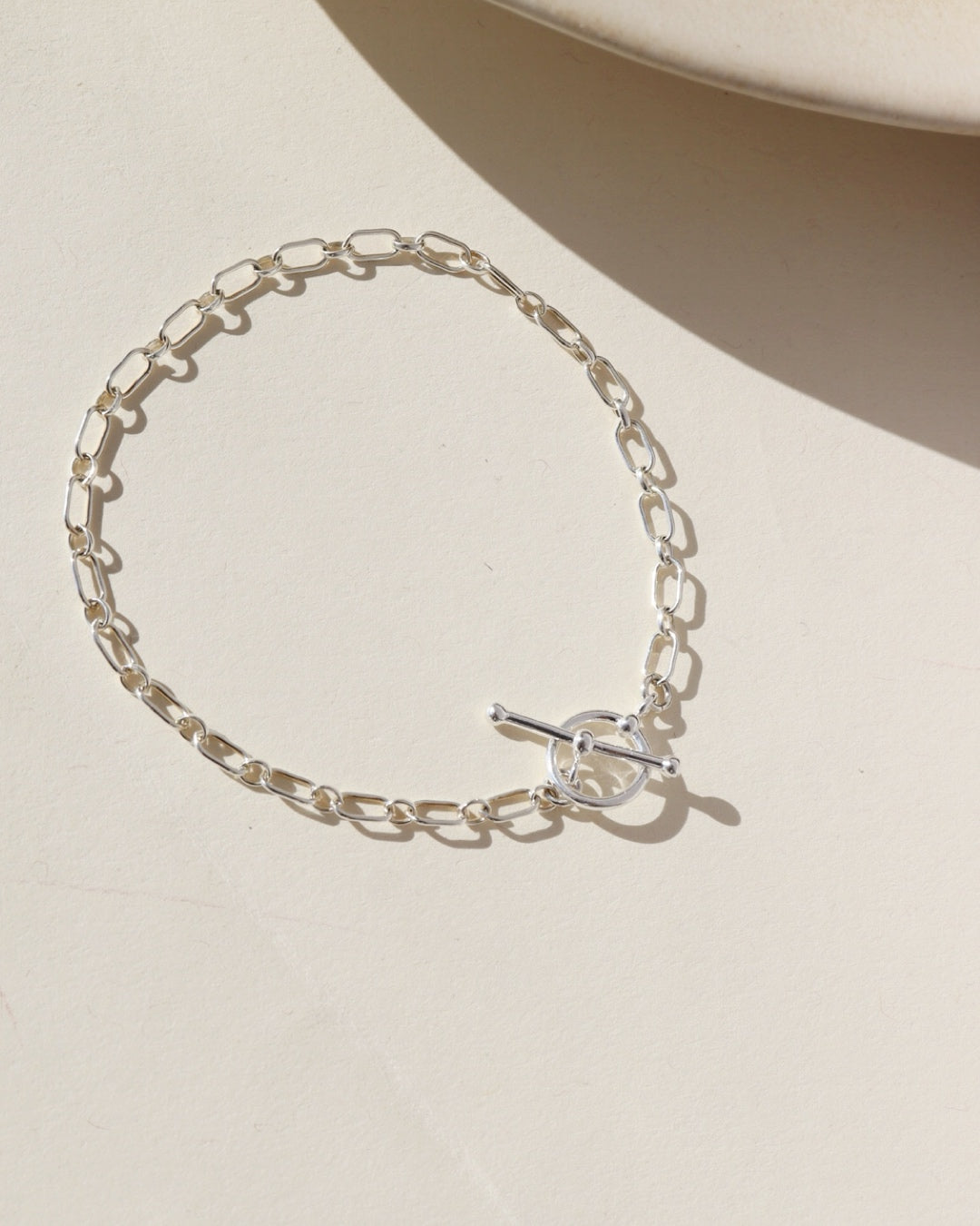 Sterling Silver Brooklyn Toggle Bracelet featuring elongated chain links and a front toggle clasp, styled on a neutral surface in natural light.