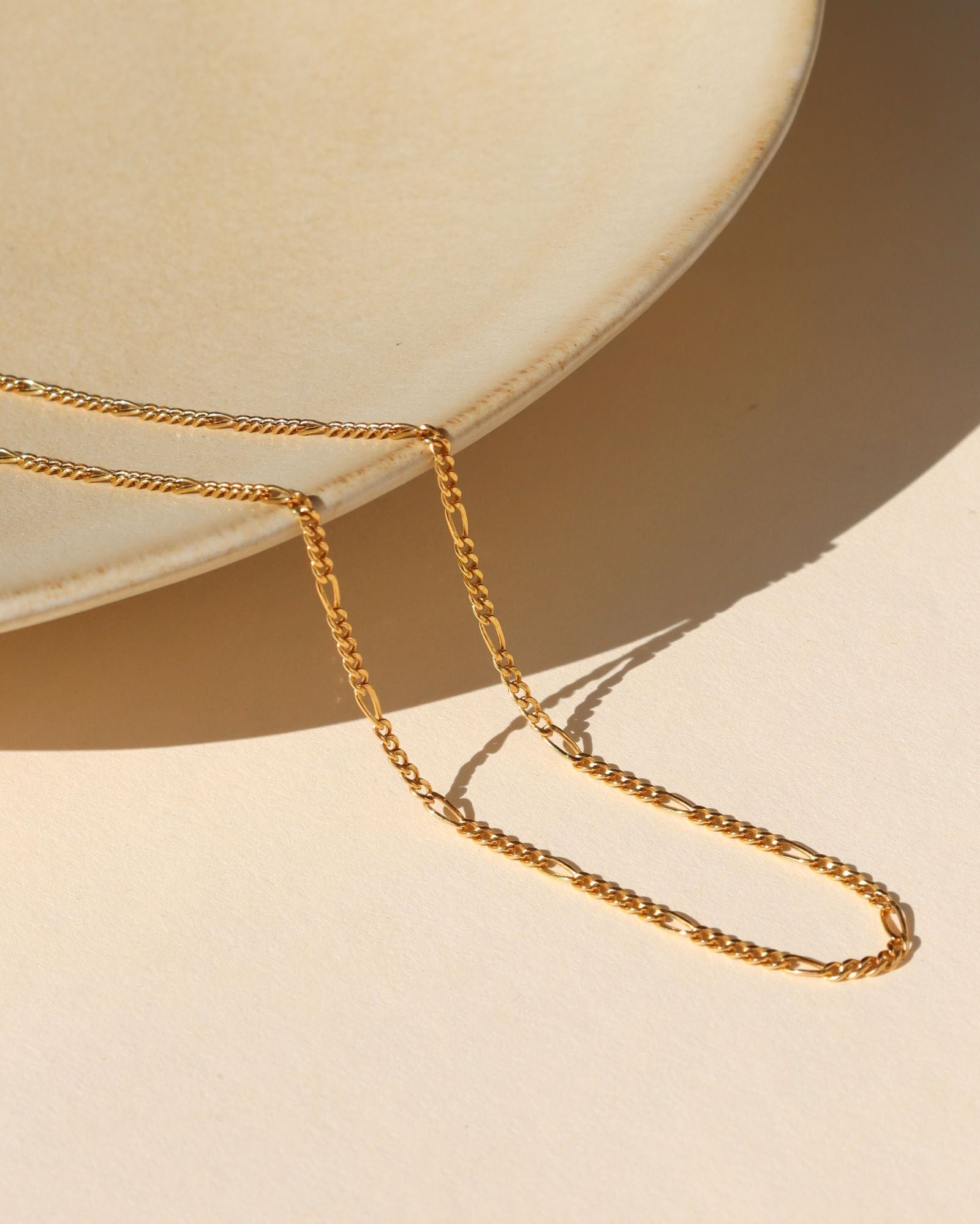 14k Gold Fill Figaro stacking chain on a light dish in the sunlight