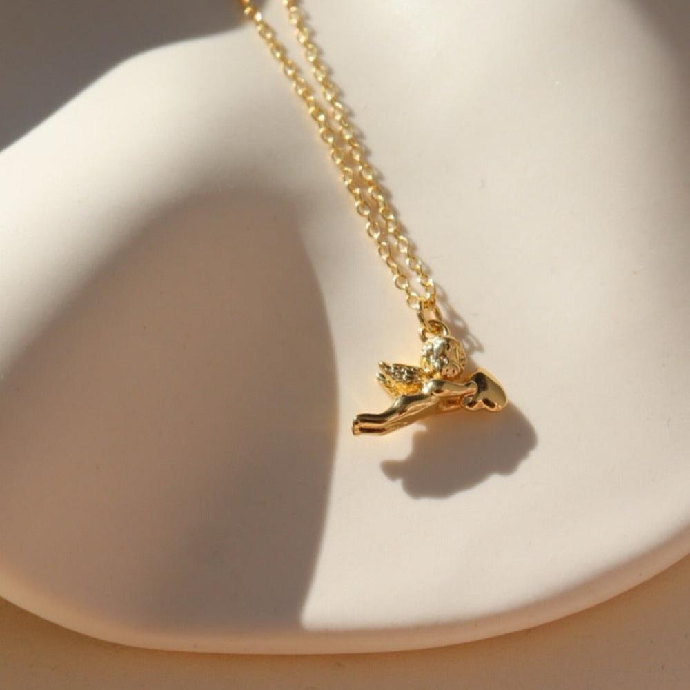 14k gold fill necklace with a thin standard chain with a cupid gold charm at the end of chain. Necklace is displayed on a white dish. 