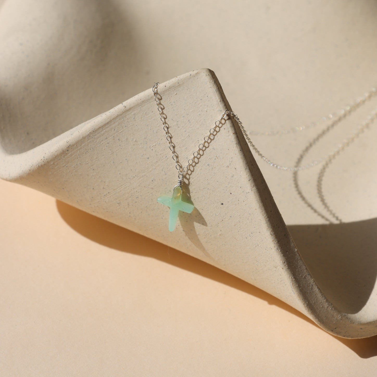 sterling silver delicate chain necklace with Chrysoprase Cross charm on a light dish