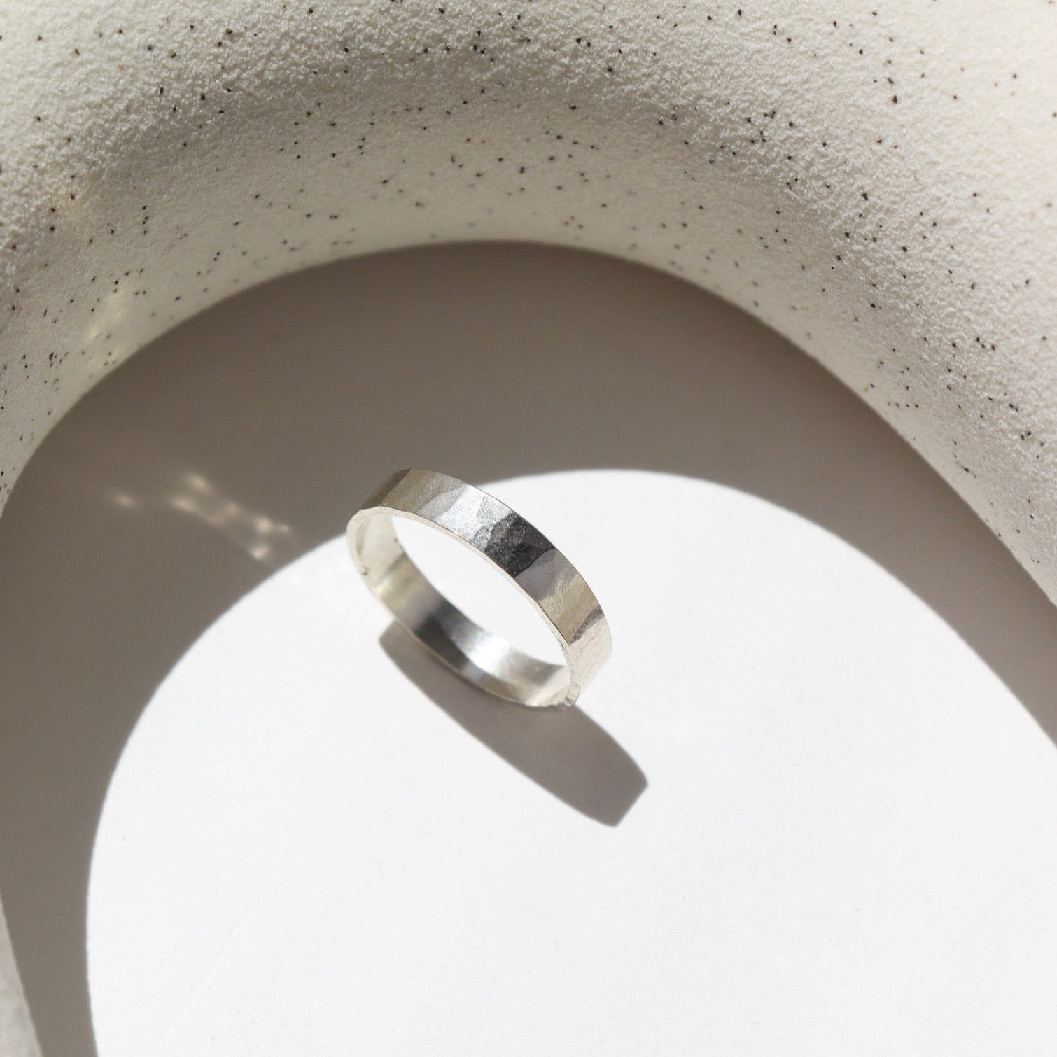 925 sterling silver cigar style ring laid on a white plate in the sunlight. This ring features a hammered band