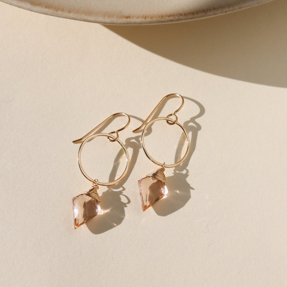 Gold earrings with rose quartz stones on a beige surface