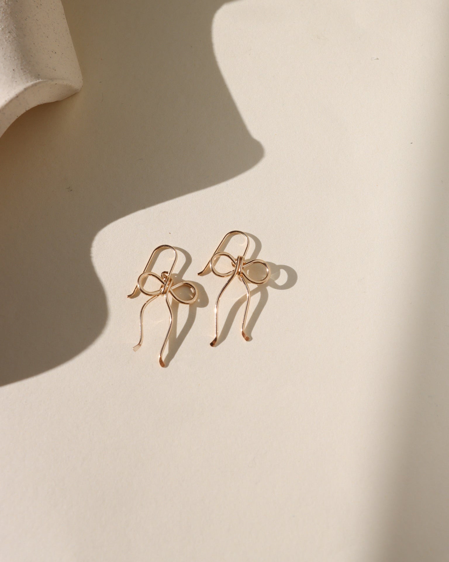 14k gold fill hand shaped bow earrings on french ear wire on a light background