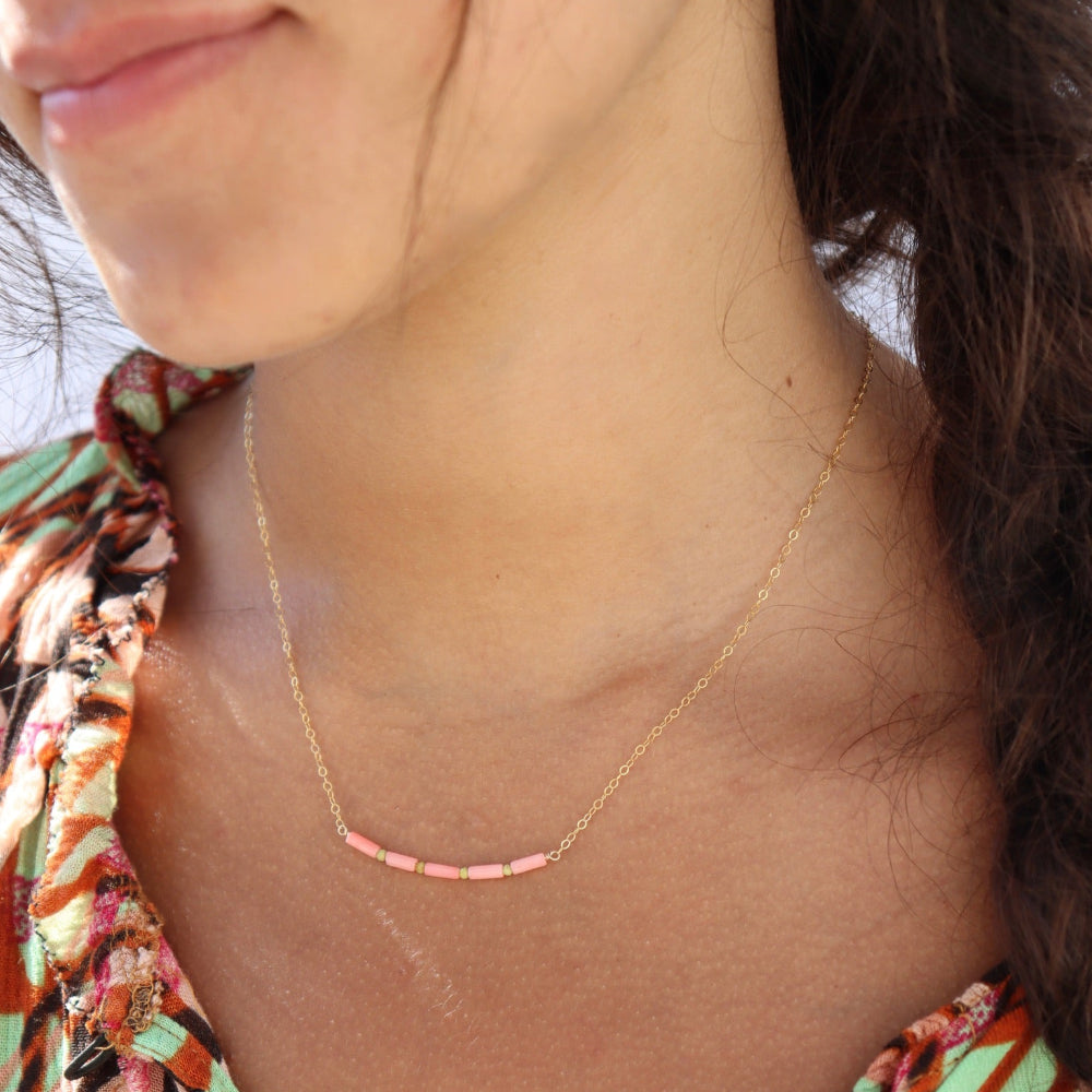 Model wearing a 14k gold-filled necklace with five coral tube gemstones and serpentine beads