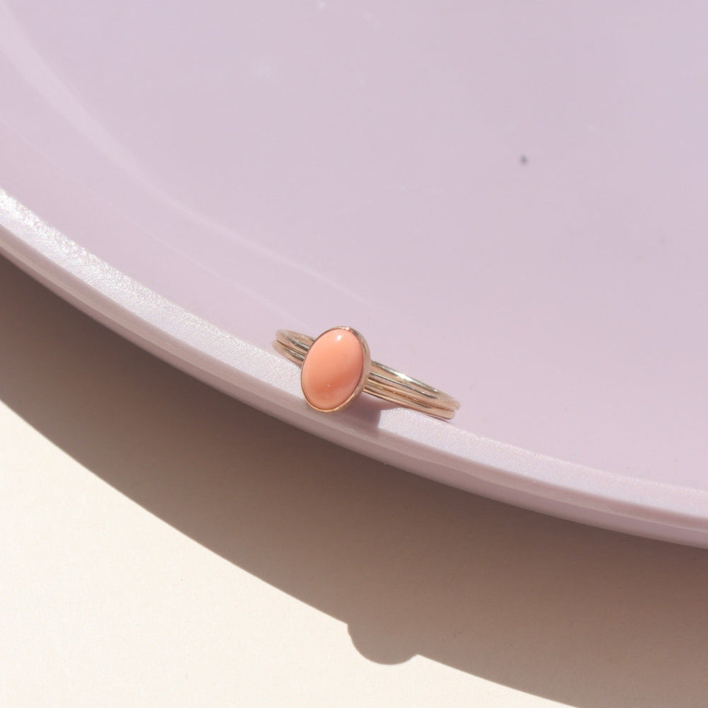 Coral gemstone set in a 14k gold fill bezel, displayed on a purple dish in natural sunlight.