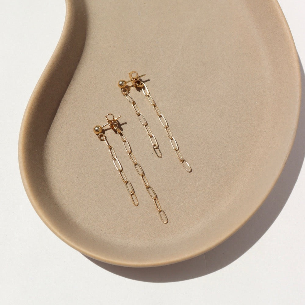 Cosette Double Drop Earrings in 14k Gold laid on a tan plate in the sunlight.