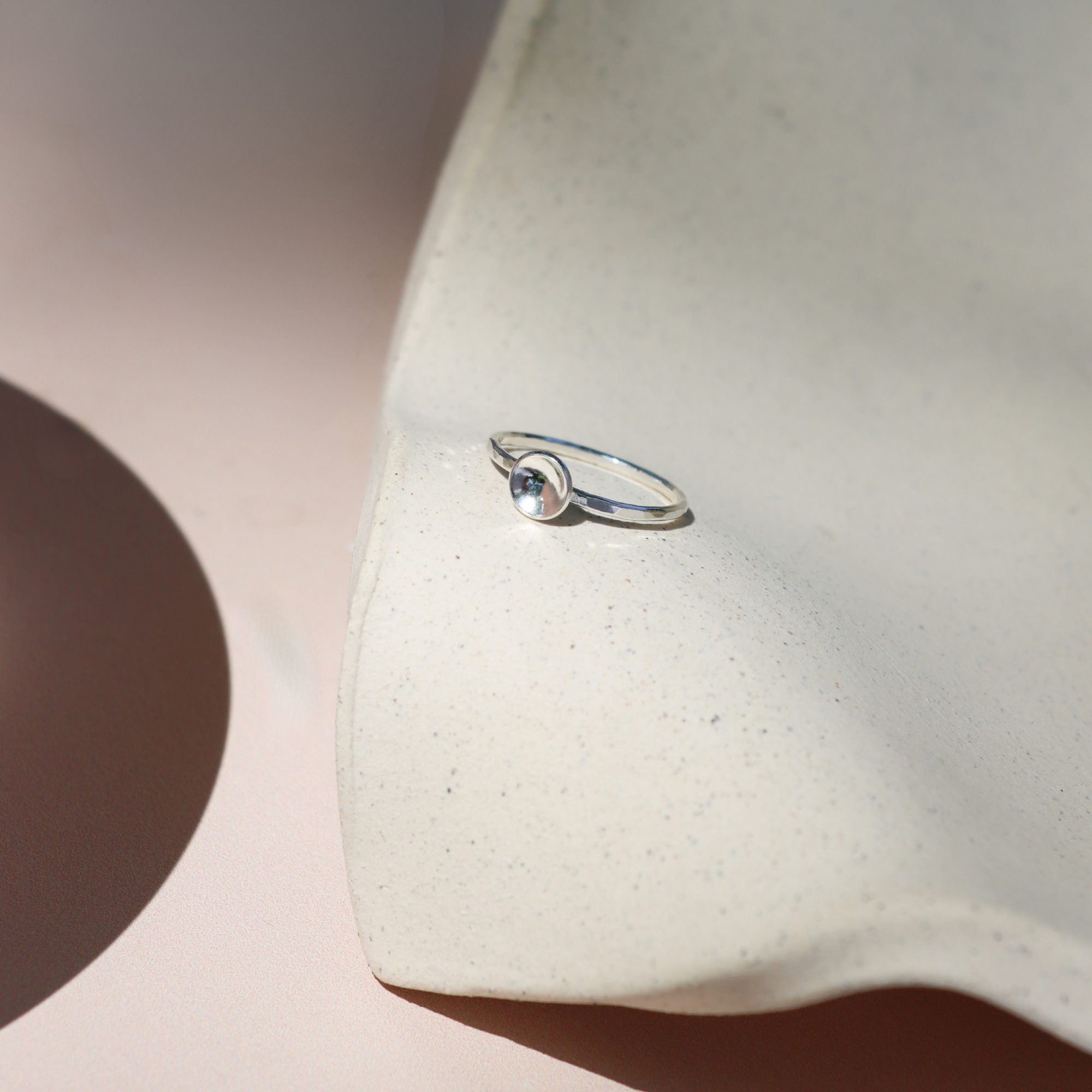 sterling silver delicate band ring with curved disc on a light dish