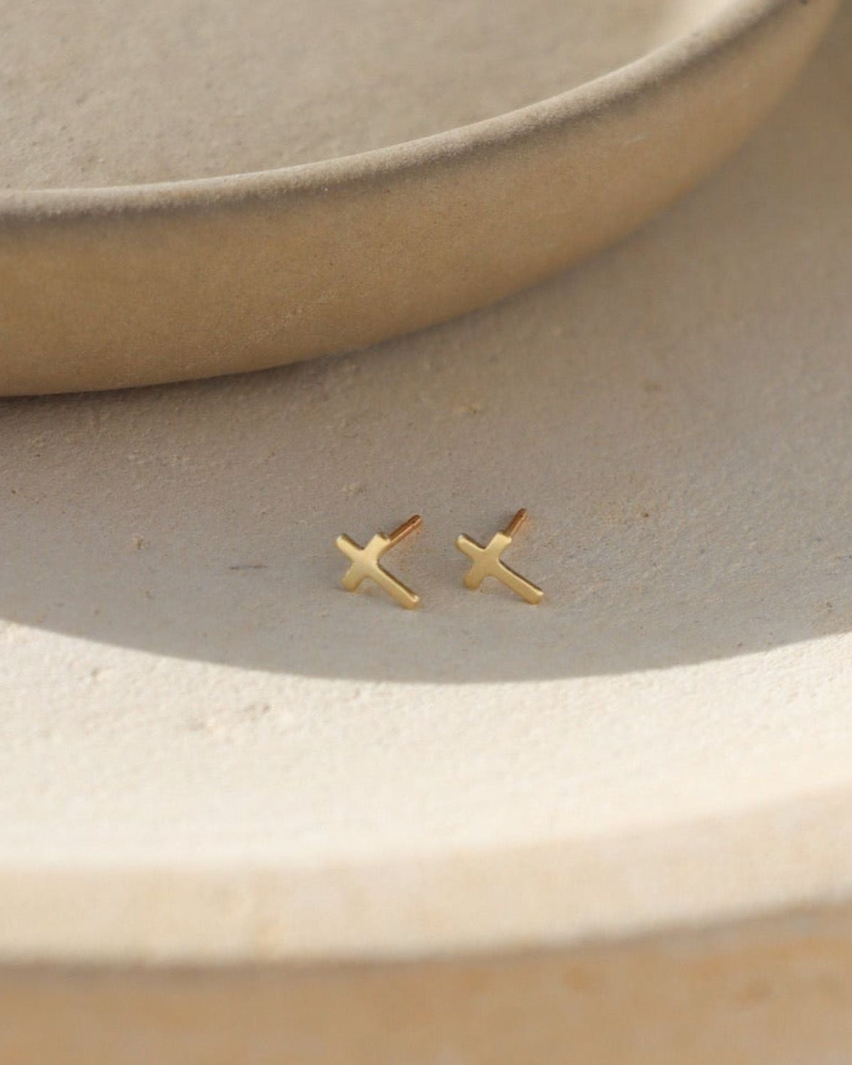 14k gold fill cross shaped studs on a light dish