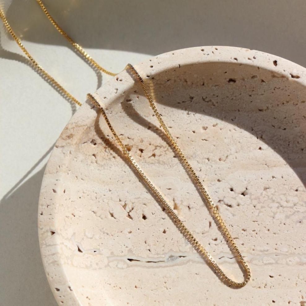 14k gold fill Necklace laid on a cream plate in the sunlight.