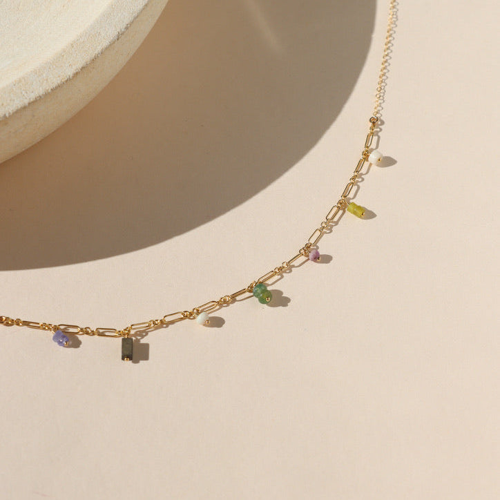 14k gold fill chain necklace with various gemstone charms by a light dish