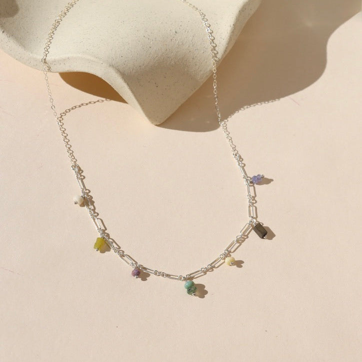 sterling silver chain necklace with various gemstone charms on a light dish